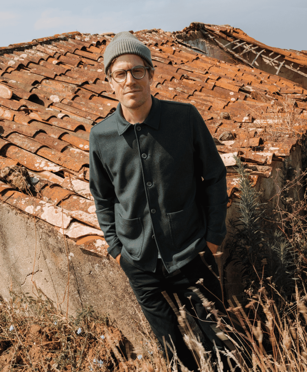 Man in a dark jacket and beanie standing against a sunlit terracotta roof