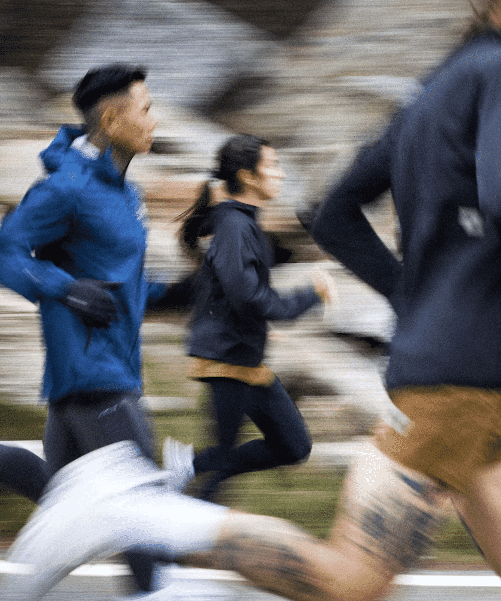 A motion-blurred shot of three runners in athletic wear sprinting on a city path.