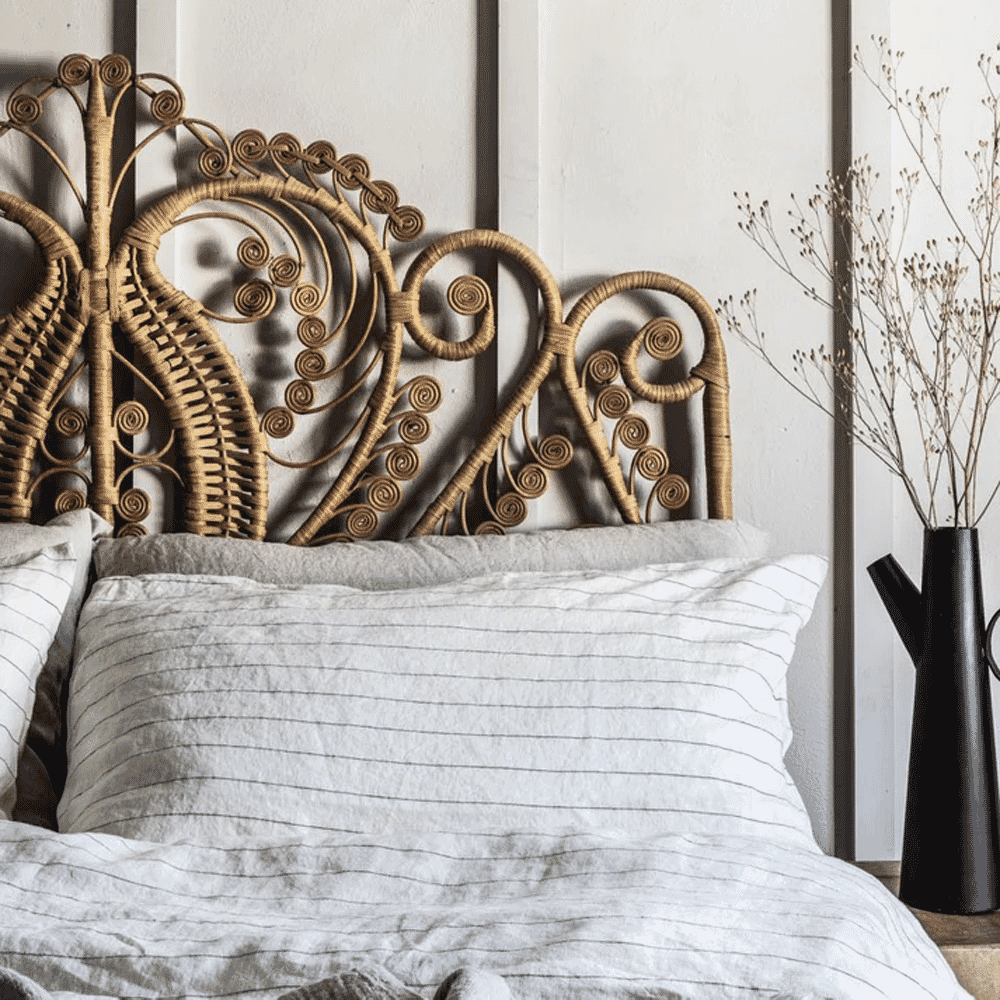 Bohemian bedroom with a rattan headboard and neutral striped linen bedding.