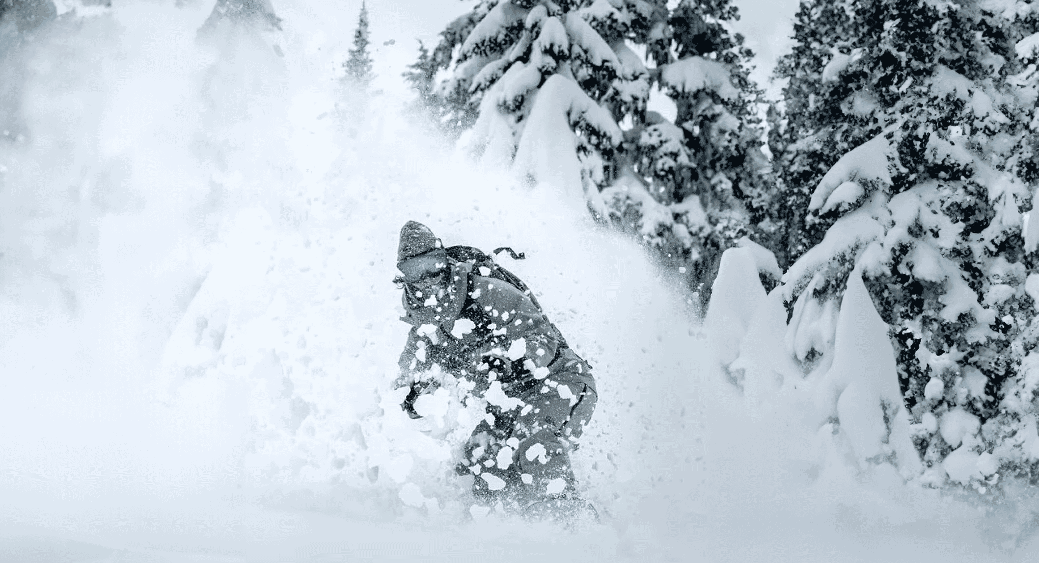 Snowboarder navigating through deep powder snow in a rugged mountain setting.