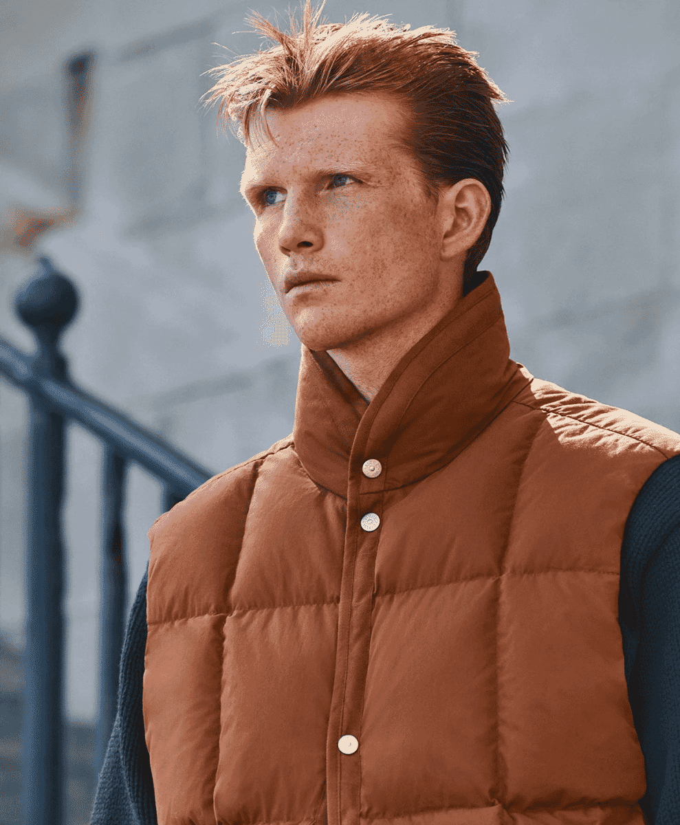 A man with red hair wearing a brown quilted puffer vest over a dark sweater.