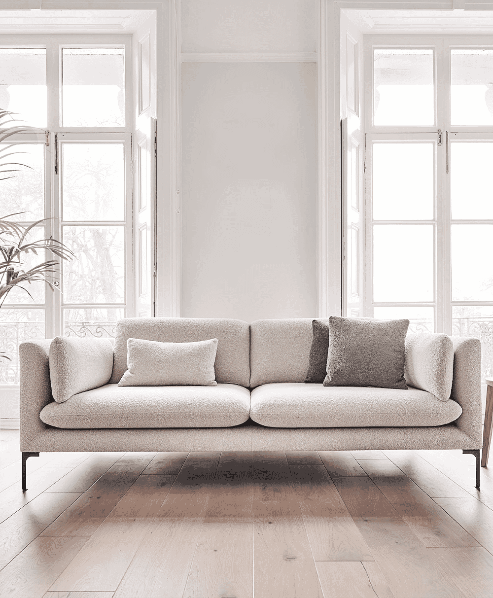 Light-colored bouclé sofa with textured cushions in a bright room with wooden floors.