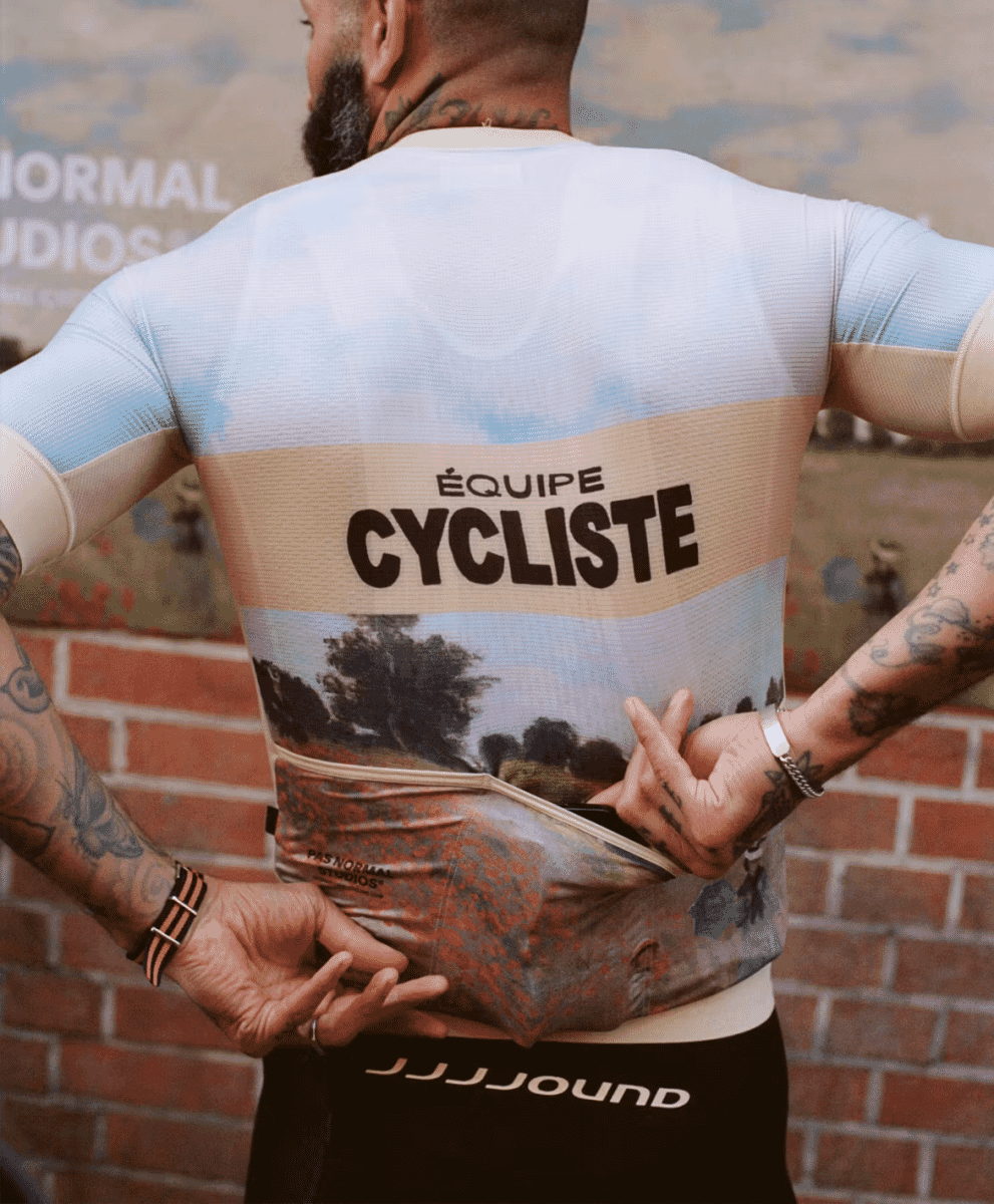 Close-up of a man wearing a cycling jersey featuring a detailed landscape painting print and 'ÉQUIPE CYCLISTE' text.