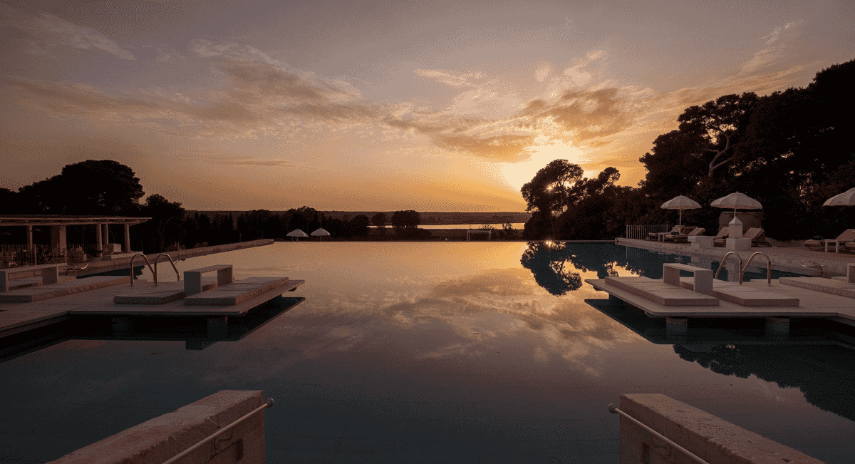 Luxury infinity pool reflecting a golden sunset with surrounding lounge chairs.