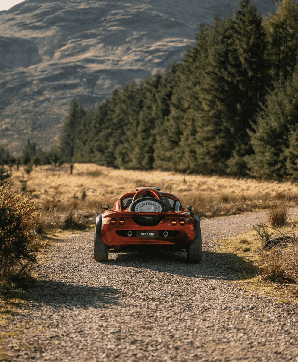 A vibrant red open-top sports car driving aggressively down a gravel mountain road.
