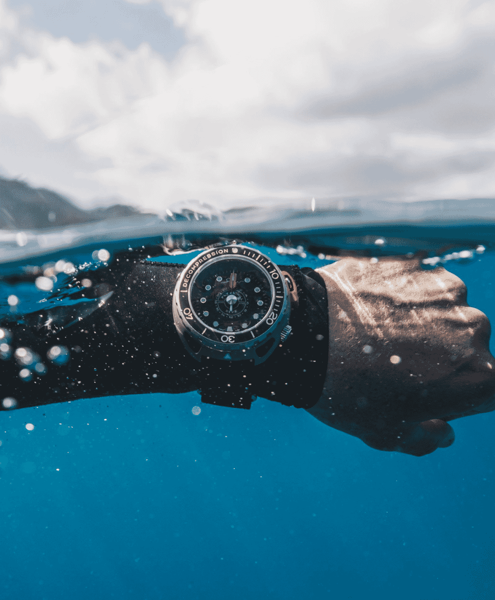 A diver's wrist submerged in water under a cloudy sky, showcasing a dive watch.