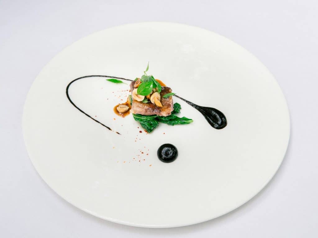 A meticulously plated gourmet dish with seared meat and micro-greens on a white plate.