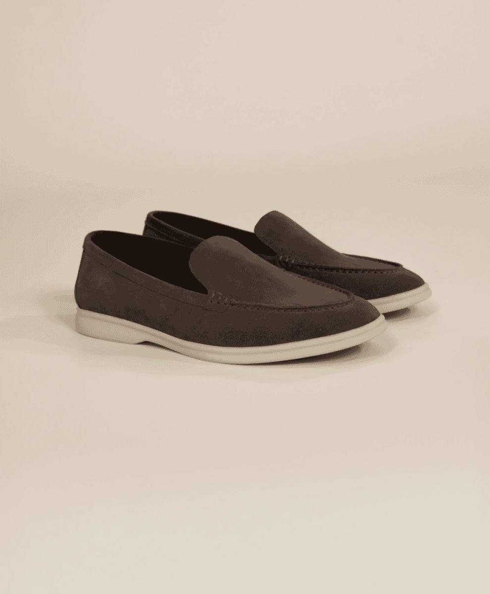 Flat lay shot of dark brown suede loafers on a beige background
