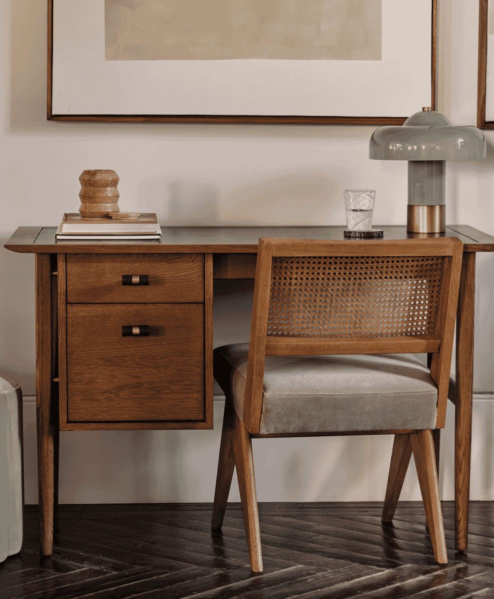Mid-century modern wooden desk paired with a cane-back chair and lifestyle decor.