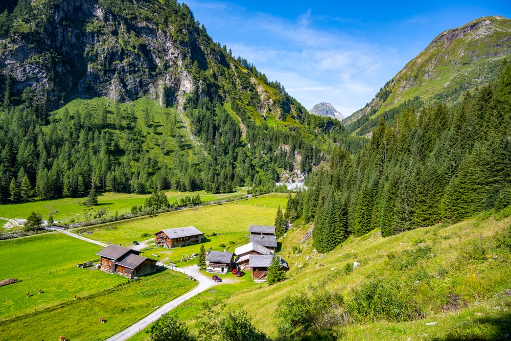 Wooden cabins nestled among forested mountains and sunny meadows in an alpine setting.