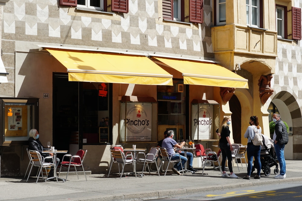 People in stylish casual attire dining at an outdoor café with distinctive yellow awnings.