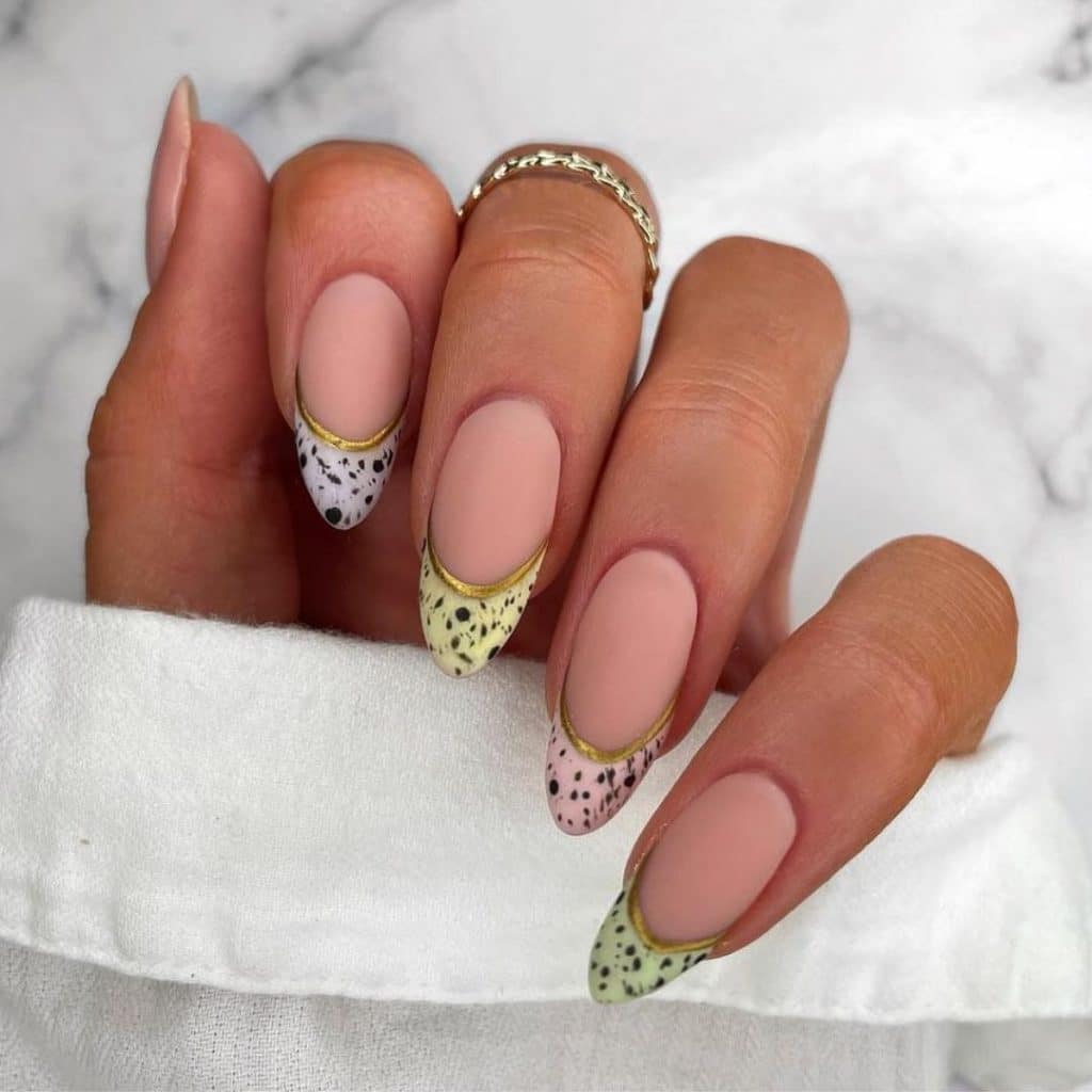 Long almond-shaped nails with matte nude polish, speckles, and gold foil.