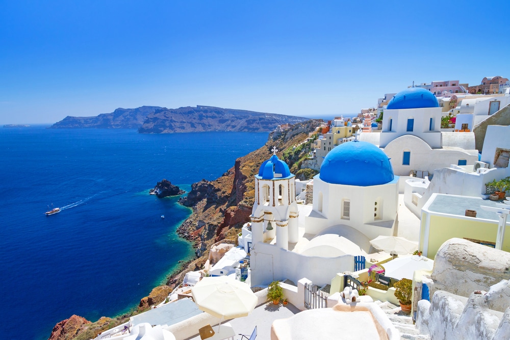 Santorini coastal village with white-washed buildings and blue domes overlooking the deep blue sea.