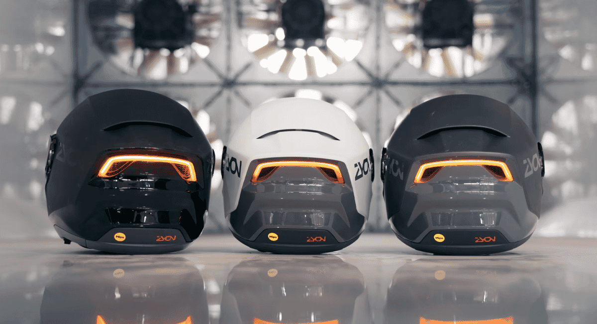 Three ZYON helmets in black, white, and gray arranged side-by-side with glowing orange rear lights.