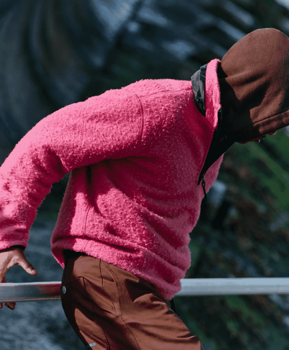 A person in a vibrant pink fleece pullover leaning on a railing.