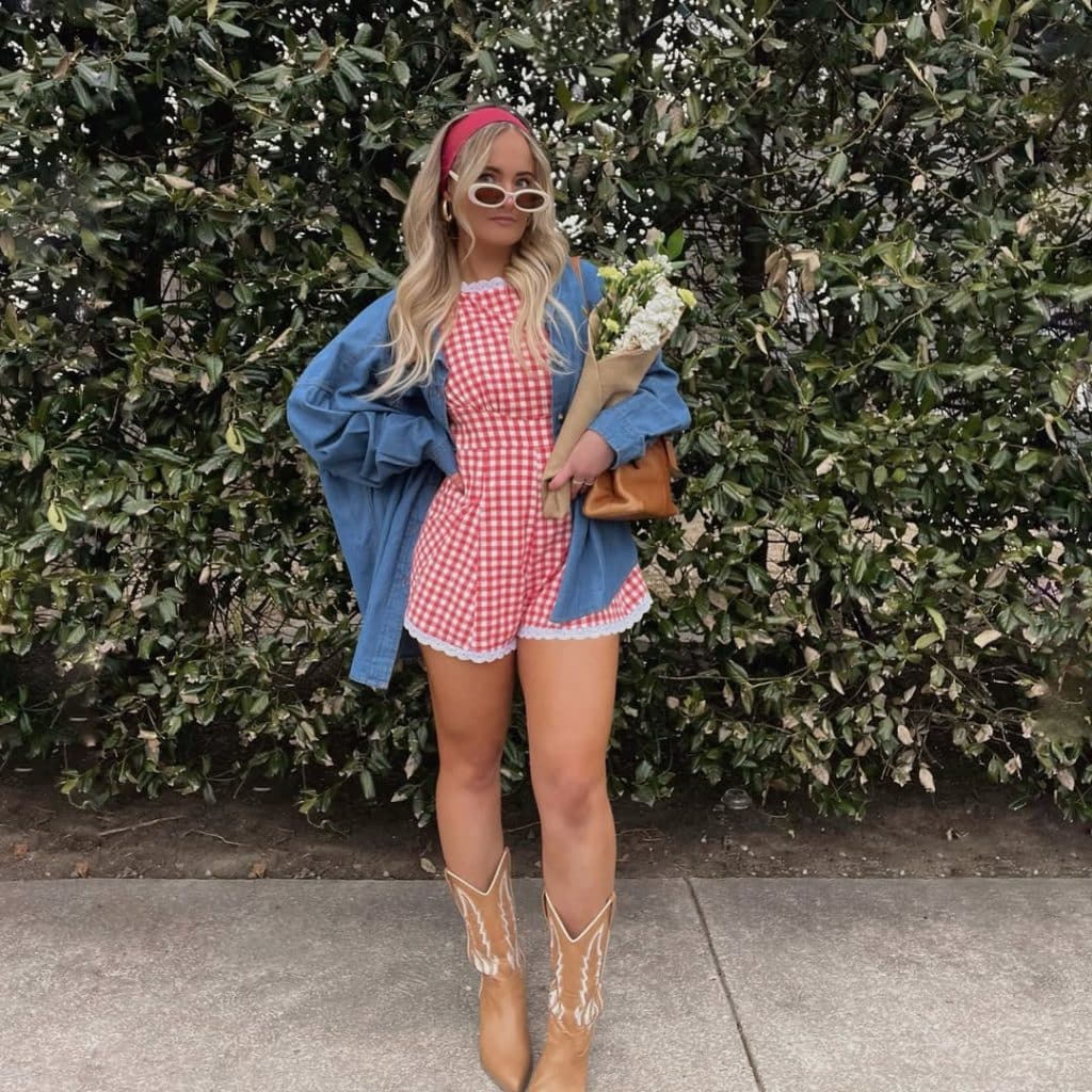Woman in a gingham romper and denim jacket holding flowers.