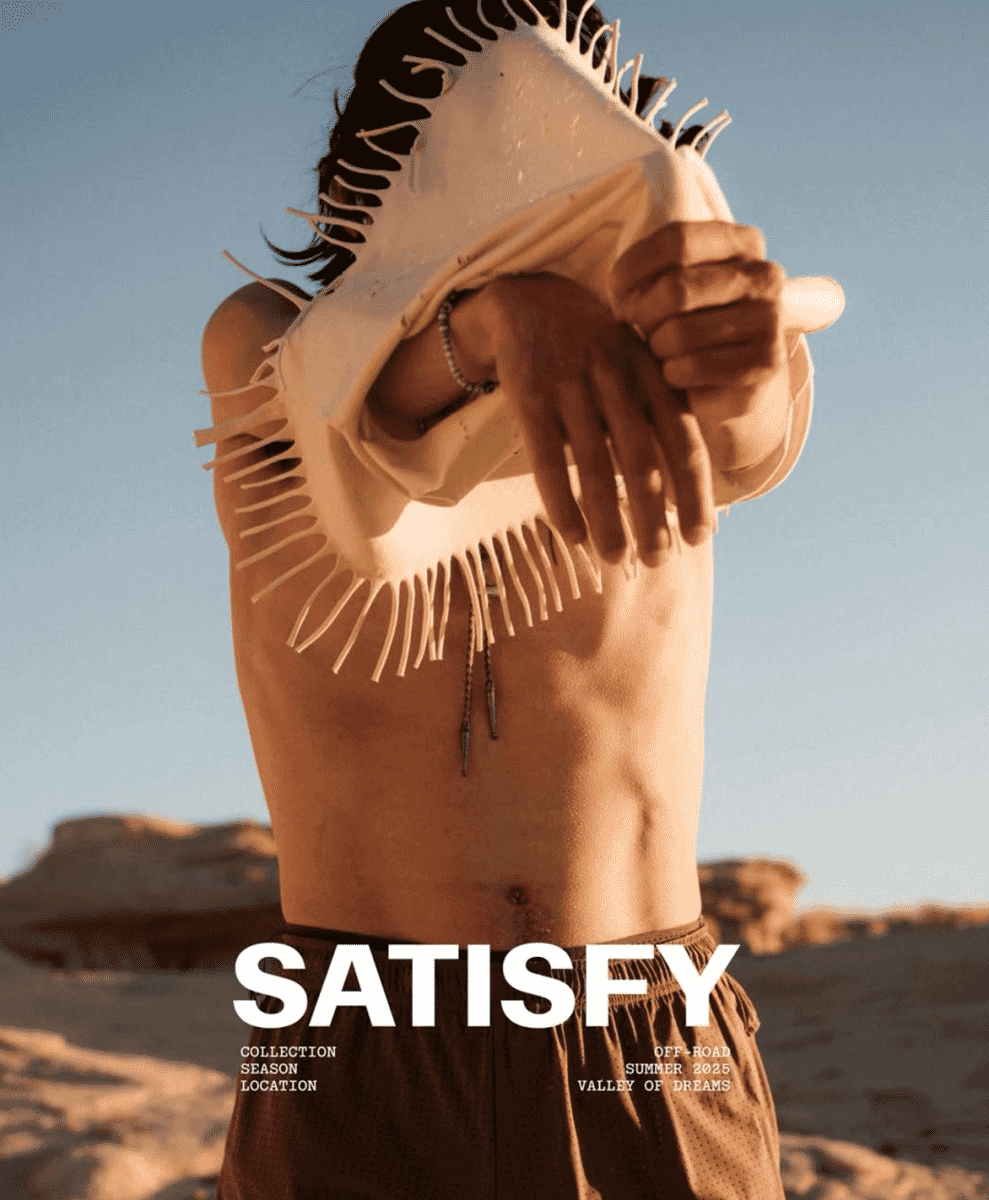 A shirtless man in a desert setting wearing white fringed headgear and brown perforated shorts.