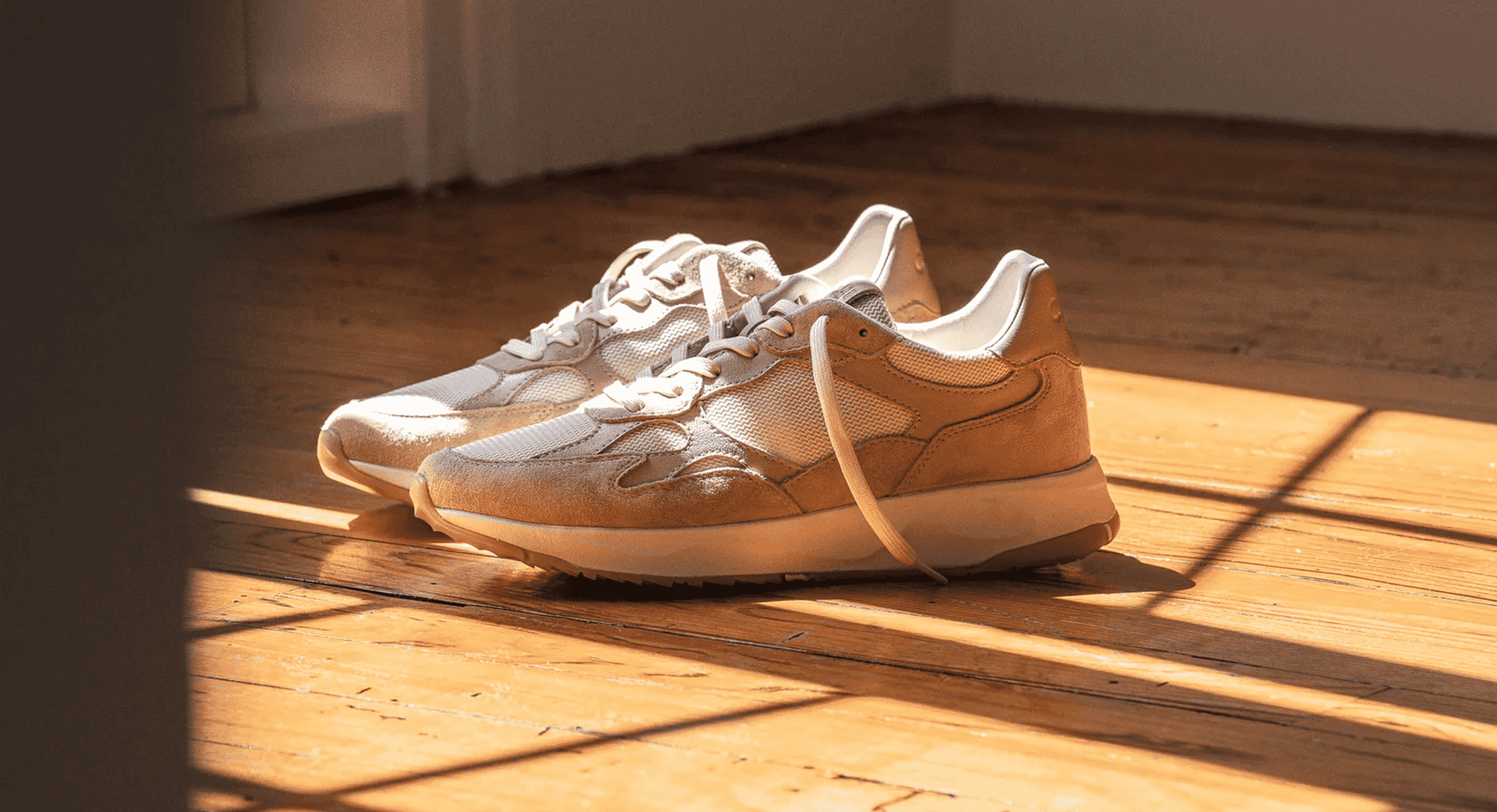 Close-up of beige and cream suede Zuma sneakers on a sunlit wooden floor.