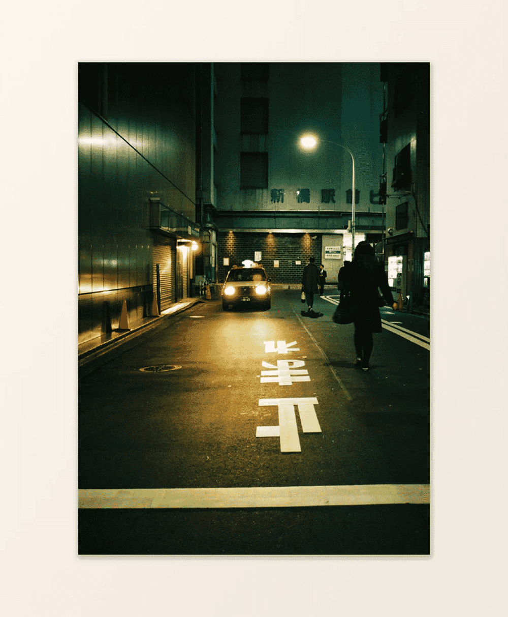 Pedestrians walking on a Tokyo street at night with Japanese characters painted on the road.