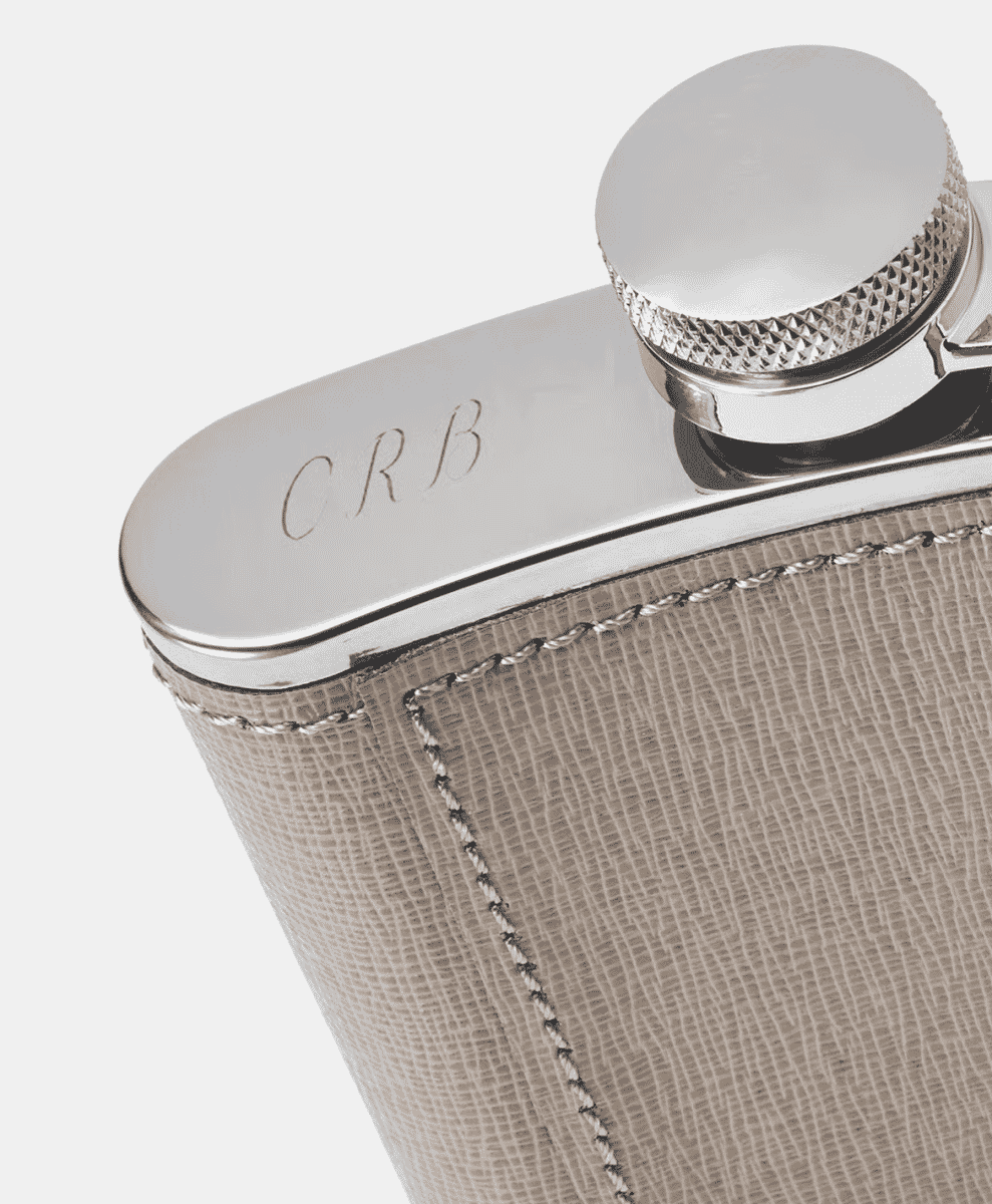 Detailed shot of a luxury leather-wrapped hip flask with 'CRB' initials engraved.