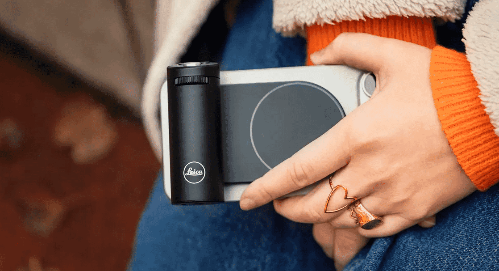 Close-up of a person in a cozy orange ribbed sweater holding the Leica grip, emphasizing hand placement and rings.
