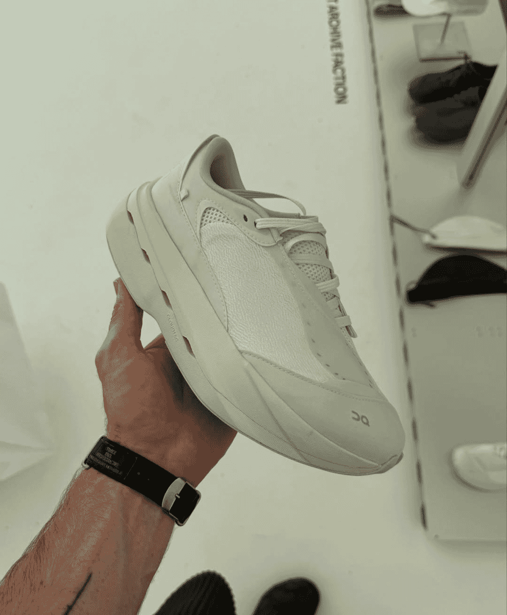 Close-up of the white ON x PAF sneaker held by a person in a retail environment.
