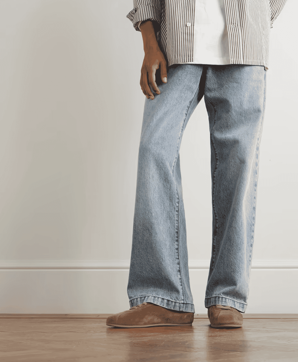 Studio shot of a person in light-wash wide-leg jeans and brown suede shoes.
