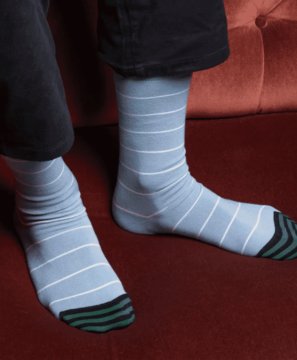 Light blue striped socks paired with dark trousers on a red velvet couch.