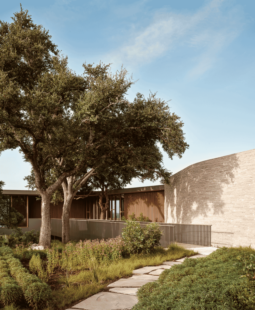 Exterior view of the residence showing a curved brick wall and wooden siding surrounded by trees.