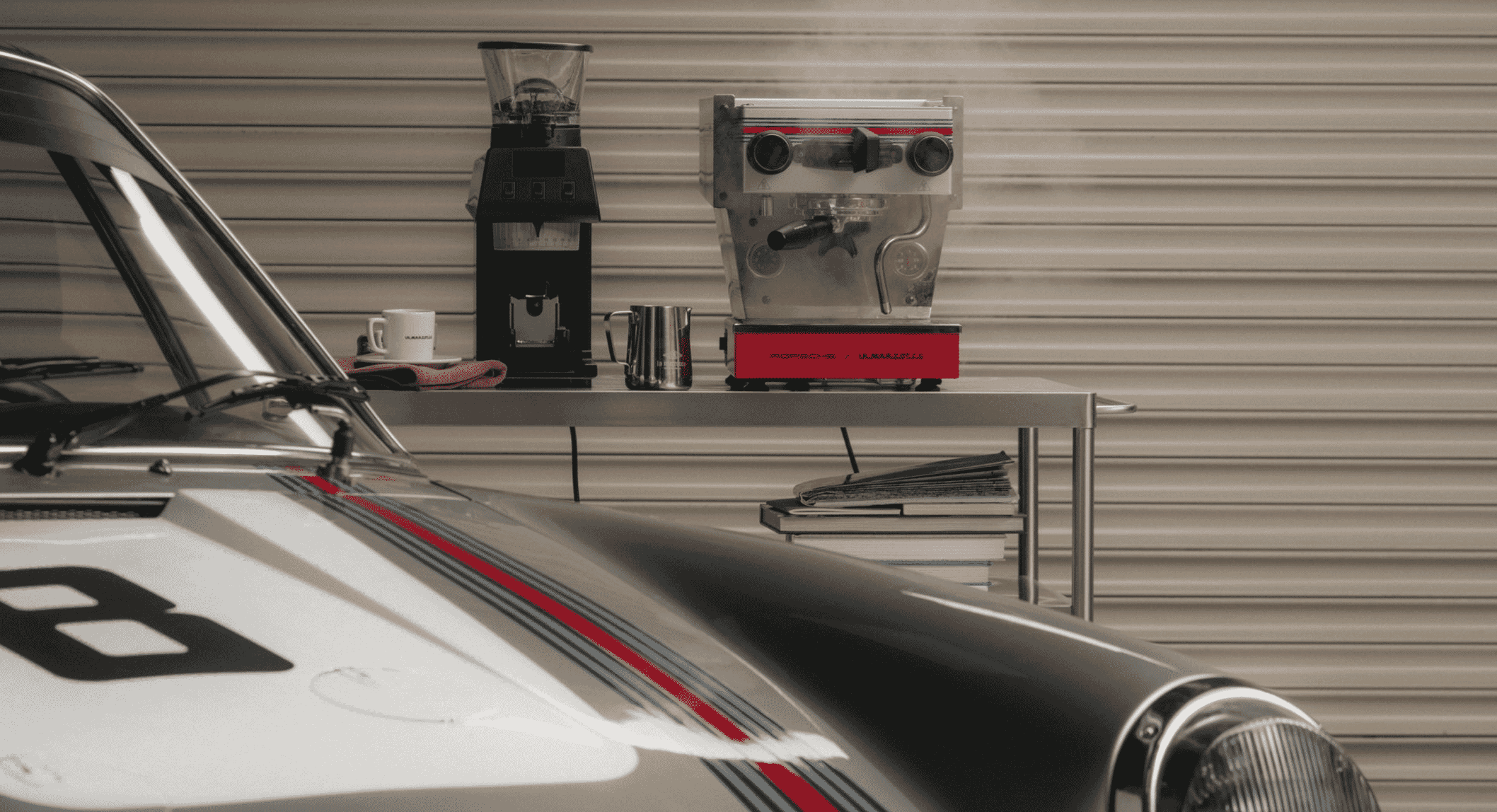 Vintage race car parked next to a coffee setup with an espresso machine in a garage.
