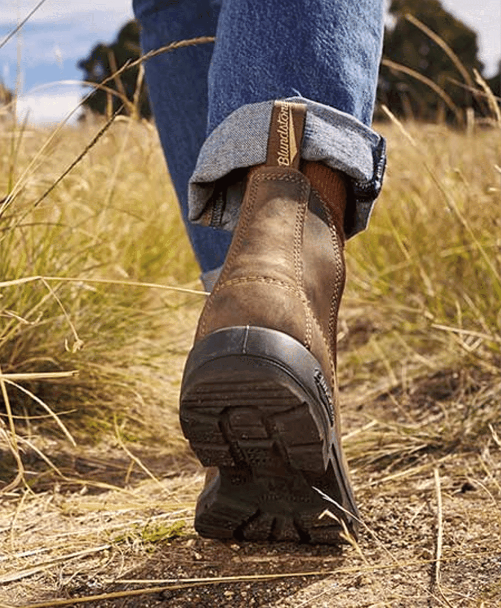 Close-up of brown Blundstone work boots and rolled-up jeans in an outdoor grassy field.