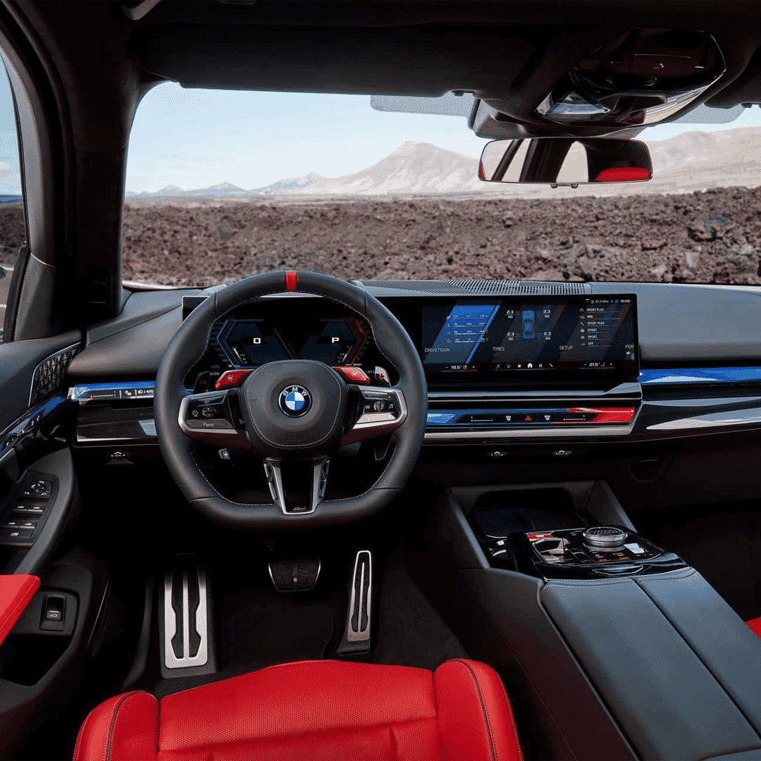 Interior view of the BMW M5 Touring with red Merino leather sport seats and a rugged mountain landscape visible through the glass.