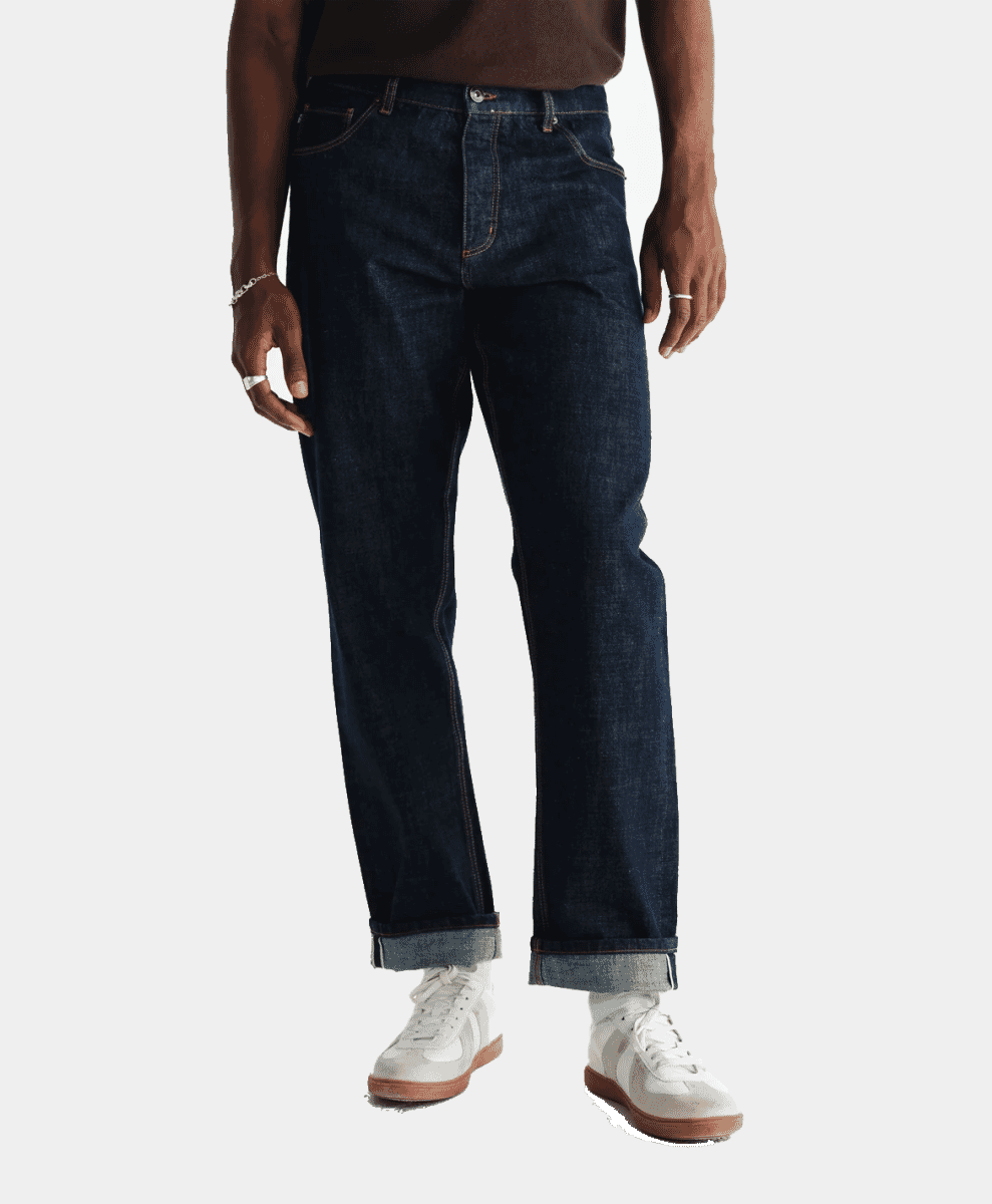 A man modeling dark blue wide-leg denim jeans with rolled cuffs.