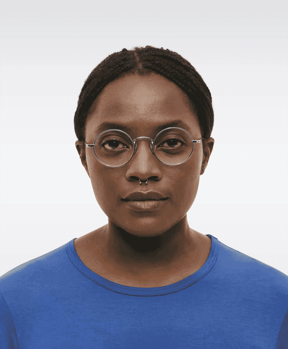 A woman wearing round metal-rimmed glasses and a simple blue shirt.