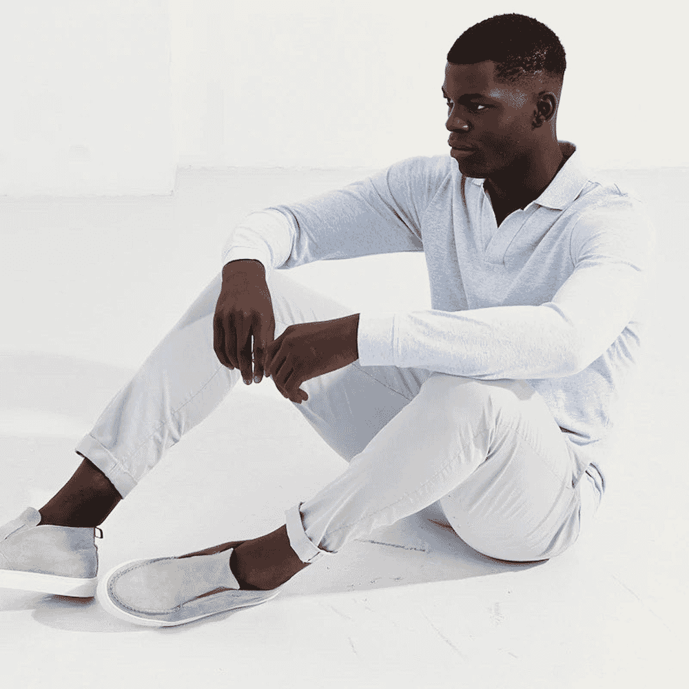 Man in a monochromatic white ensemble including a long-sleeve polo and slip-on sneakers.