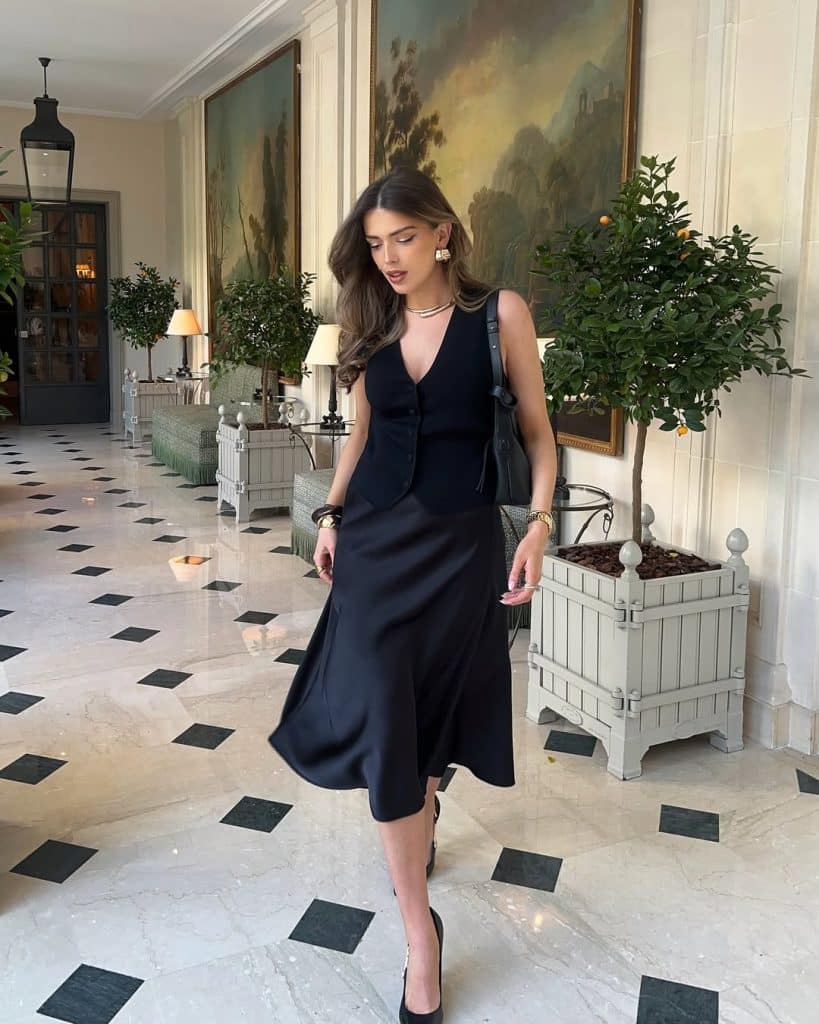 Woman in a chic black sleeveless vest dress walking through an elegant hallway.