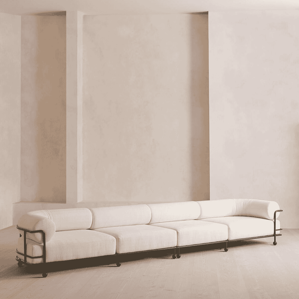 A sleek white modular sofa with a black metal frame in a minimalist, light-filled interior space.