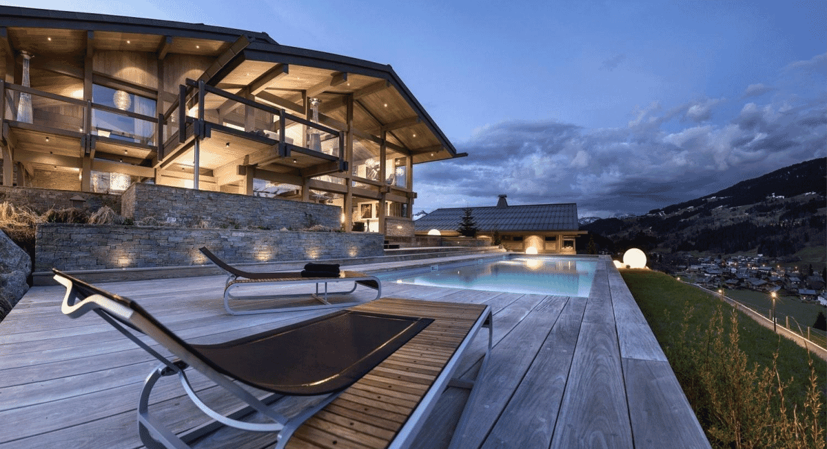 A modern luxury villa featuring a rooftop pool and deck with mountain views at dusk.