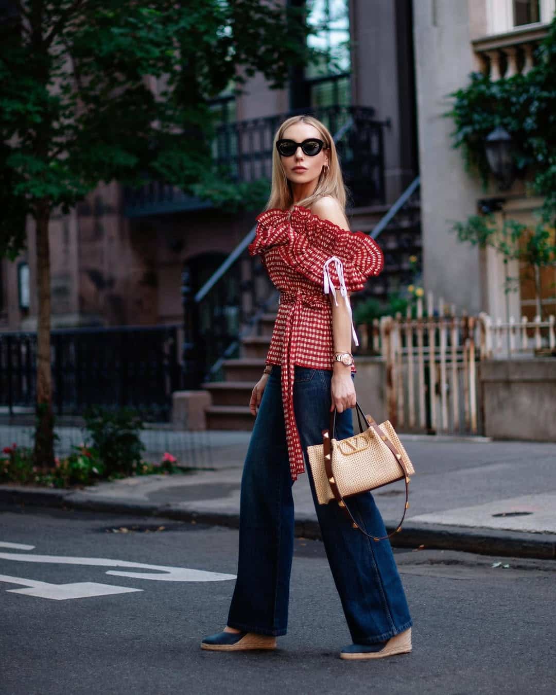 Woman in a red ruffled gingham top and wide-leg jeans walking down a street.