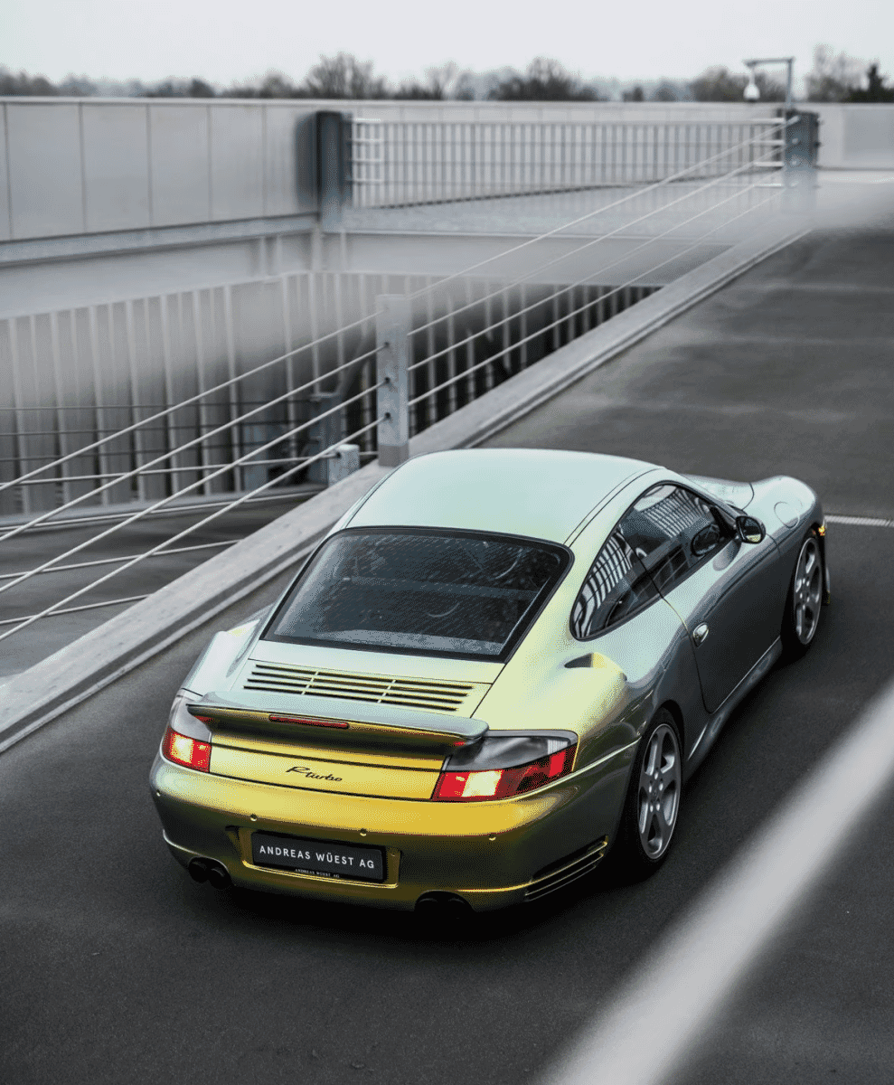 High-angle rear view of a gold metallic Porsche on a modern bridge.