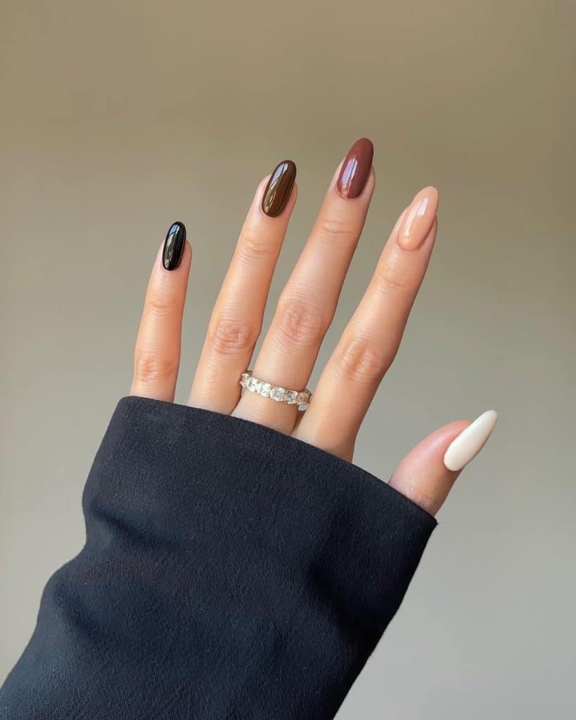 Manicured hands with brown, black, and nude glossy nails wearing a diamond ring.