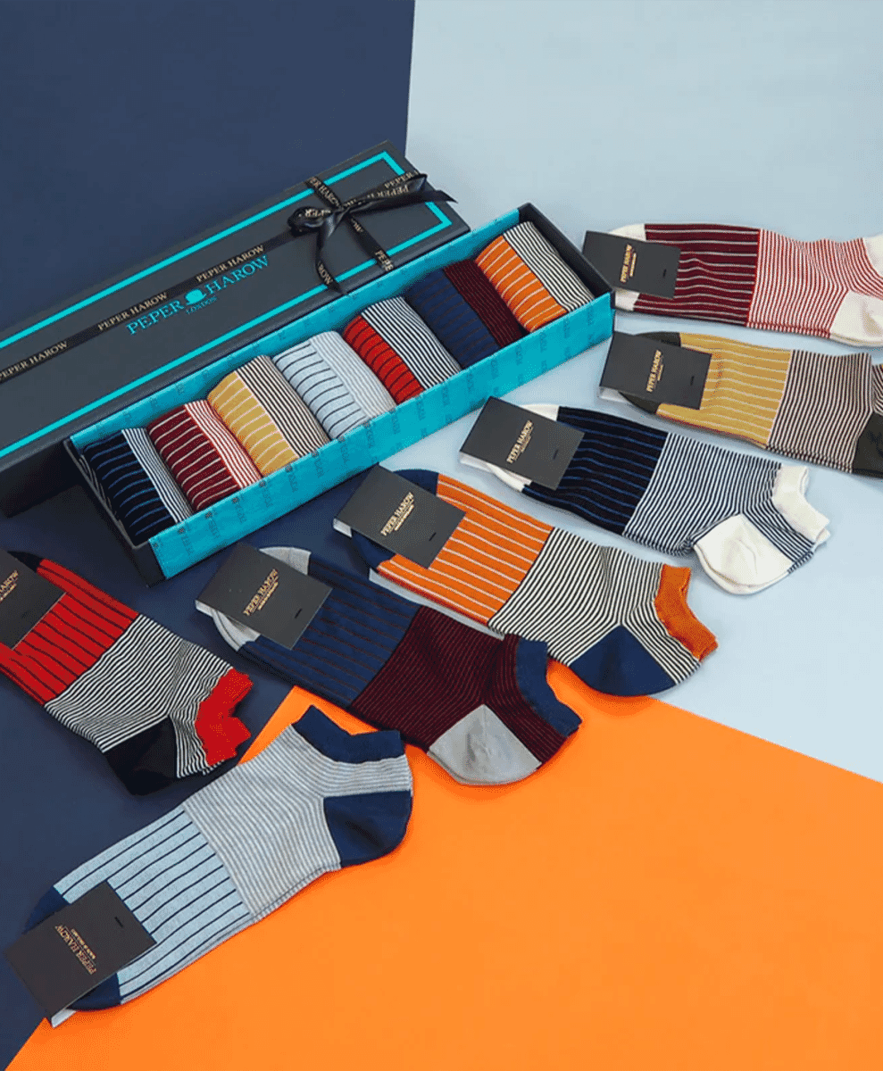 Colorful striped Peper Harow socks arranged in a gift box on a vibrant background.