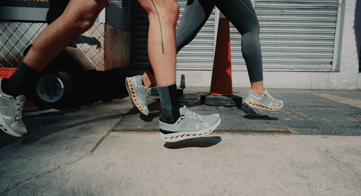 Close-up of grey-blue sneakers in motion on a city sidewalk near a storefront.