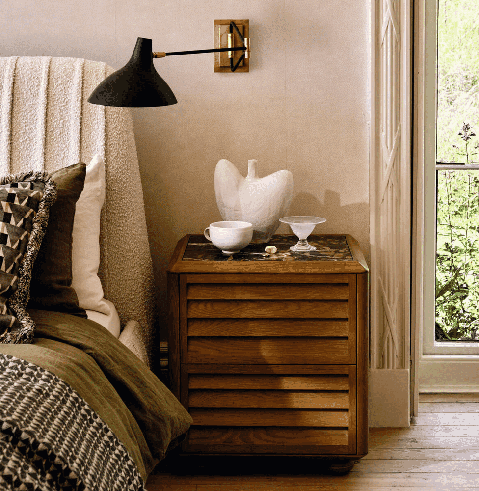 A cozy bedroom scene with soft lighting from a wall lamp illuminating textured bedding and a wooden nightstand.