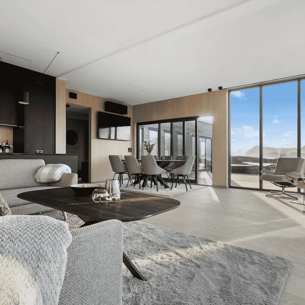 Modern minimalist living room with grey sofas and large glass windows overlooking a mountain view.