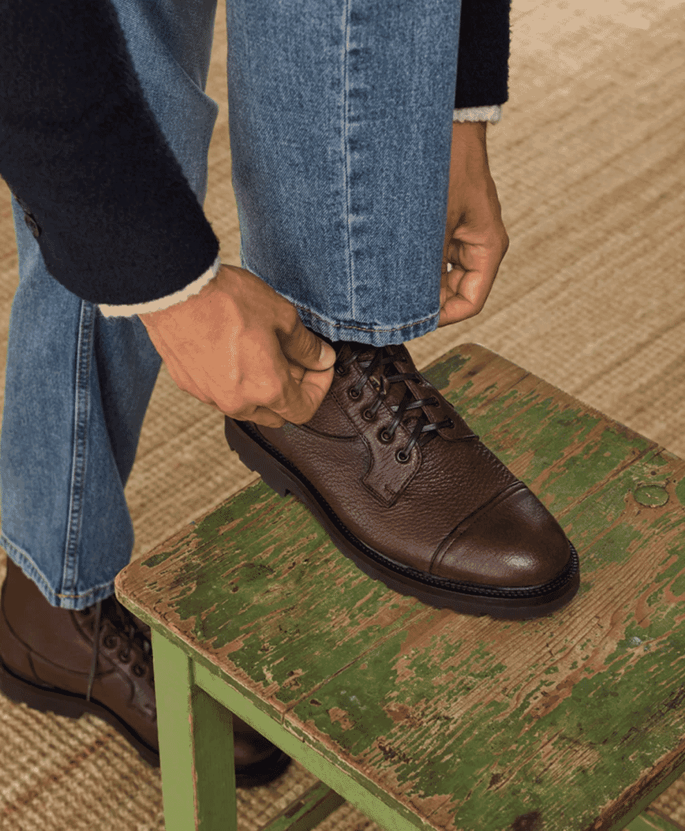 Close-up of jeans being adjusted over brown leather cap-toe dress boots.