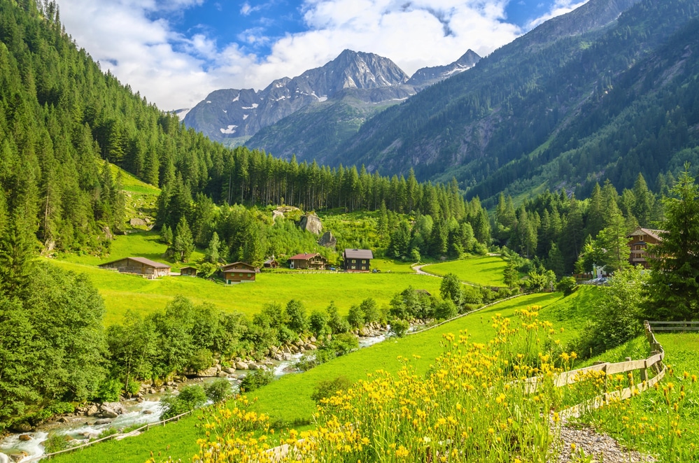 A scenic Alpine valley featuring traditional wooden chalets and lush green meadows under a blue sky.