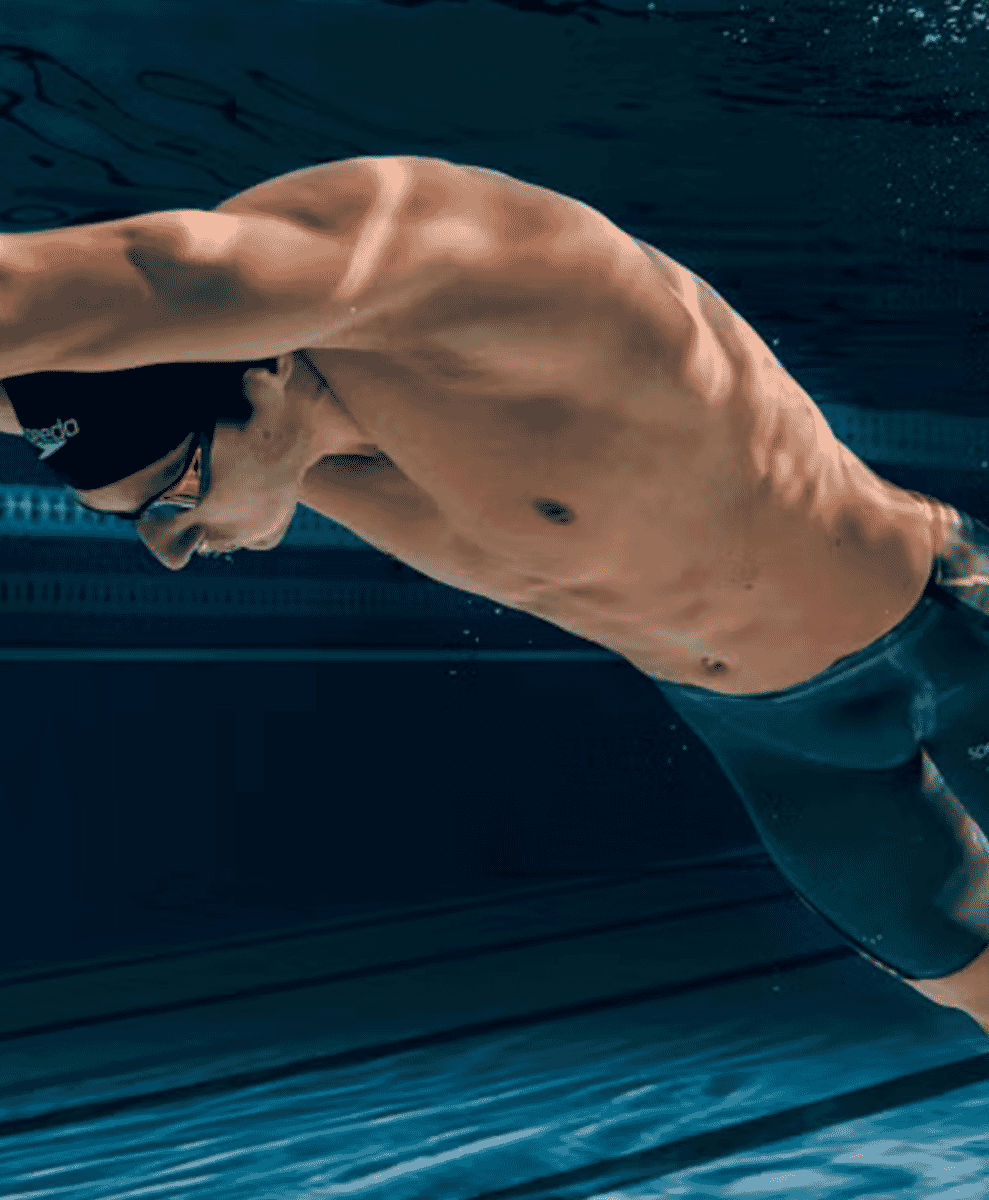 An underwater view of a swimmer in a dark Speedo cap and trunks gliding through pool water.