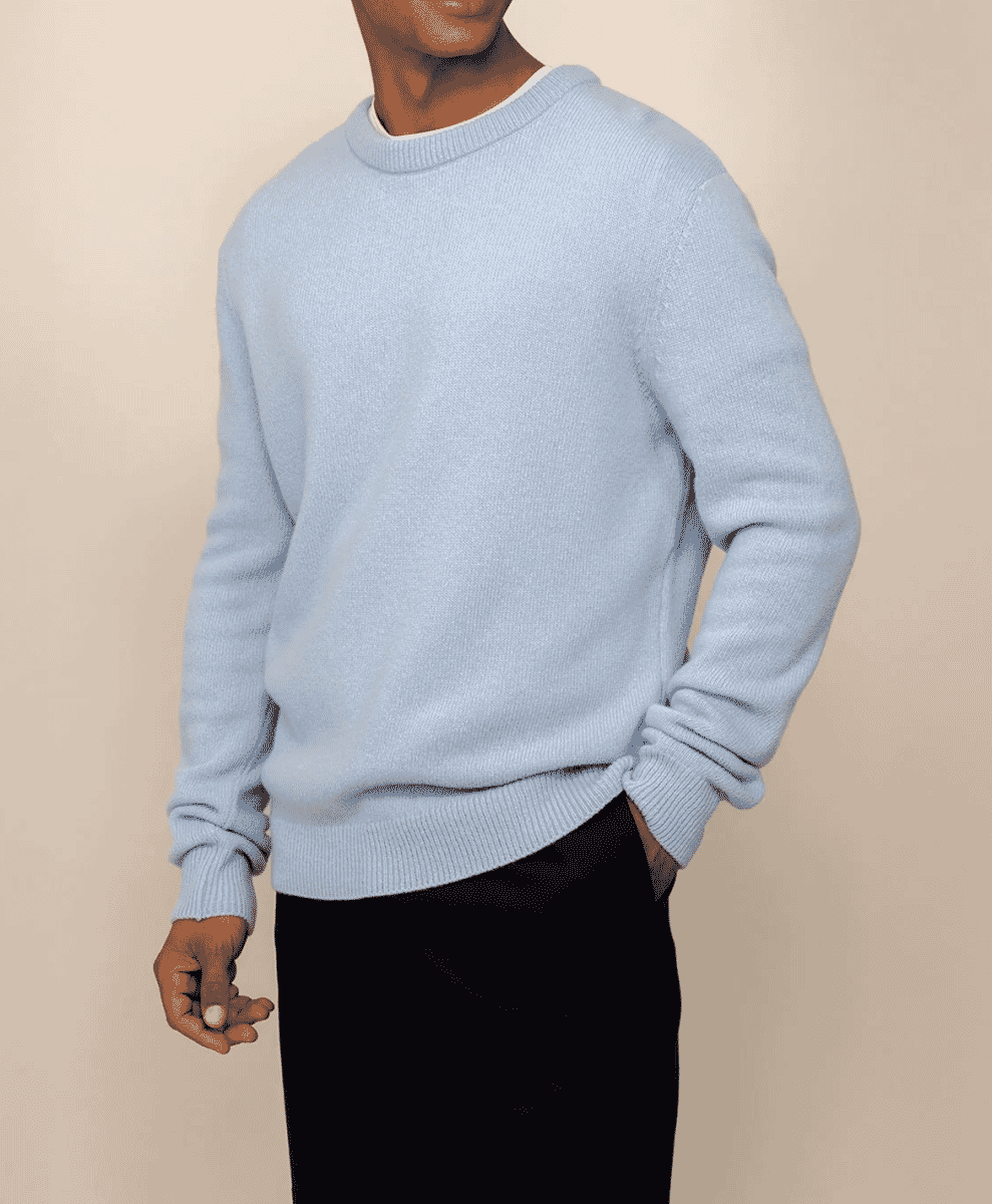A man wearing a light blue ribbed knit sweater with black trousers.