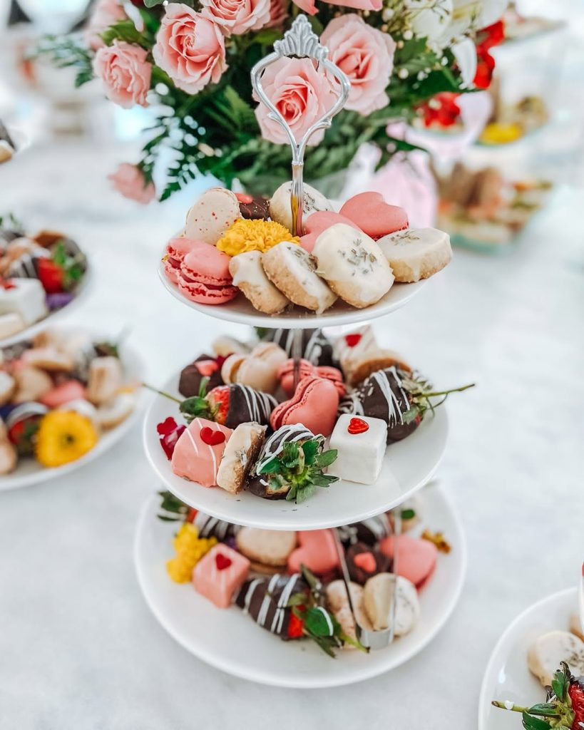 A three-tiered white stand filled with heart-shaped macarons and chocolate-covered strawberries.